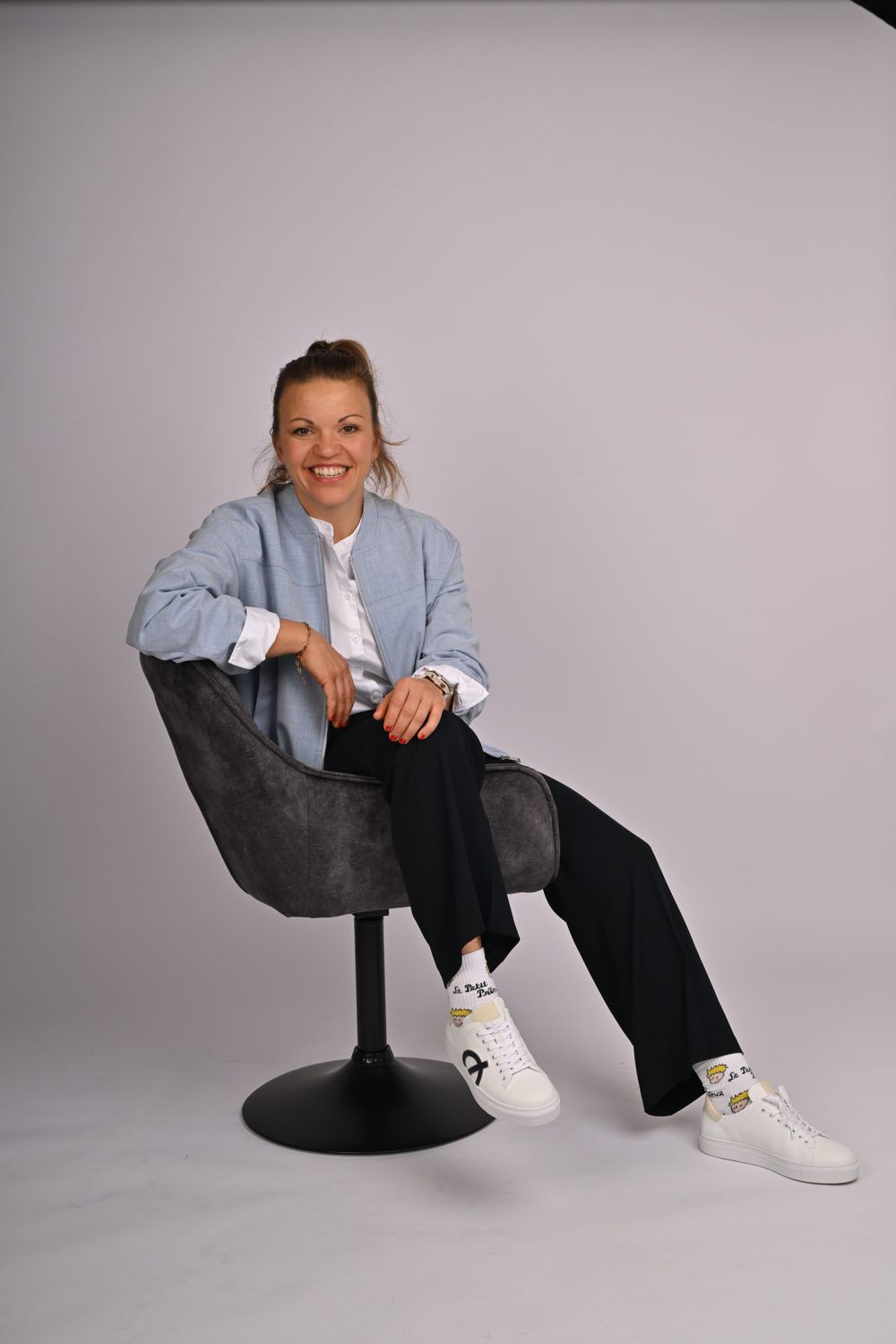 Steffi Reith in hellblauer Jacke, entspannt im Sessel sitzend